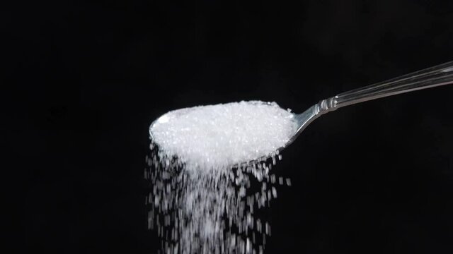 slow motion of white sugar pouring from a spoon isolated on black 