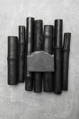 Black soap bar with bamboo charcoal and bamboo coal on grey background.