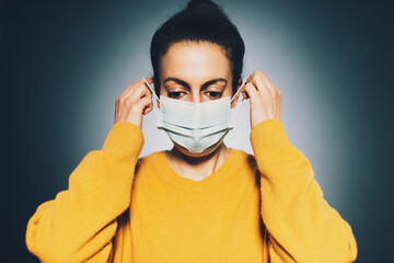 Close-up photo of young brunette woman putting on protective mask.
