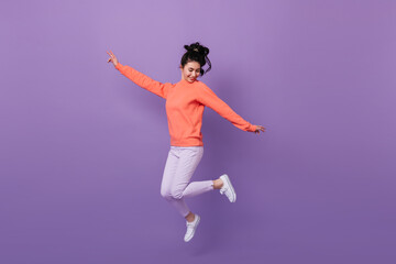 Fototapeta na wymiar Carefree pretty asian girl jumping with smile. Studio shot of funny korean woman dancing on purple background.