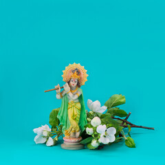 Hindu god Krishna. Statue with white apple blossoms on a blue background.