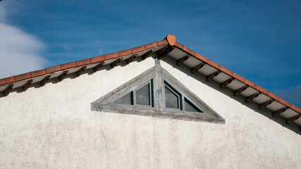 Ventana triangular en fachada blanca de casa rural con tejado de tejas de barro