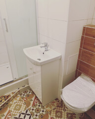 a small bathroom with colored tiles in shades of brown, a toilet with white and colored ceramic tiles, a bathroom with a shower, sink and toilet