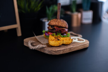 Delicious grilled hamburger and organic vegetables. Homemade beef burgers with grilled beef, mushrooms, lettuce, red onion, tomatoes and sauce on wooden cutting board as well as french fries.