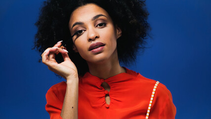 Young african american woman applying mascara isolated on blue