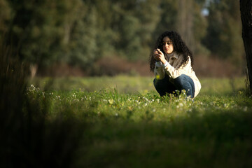 Mujer adolescente de pelo largo, moreno y rizoso recogiendo flores silvestres en el campo al...