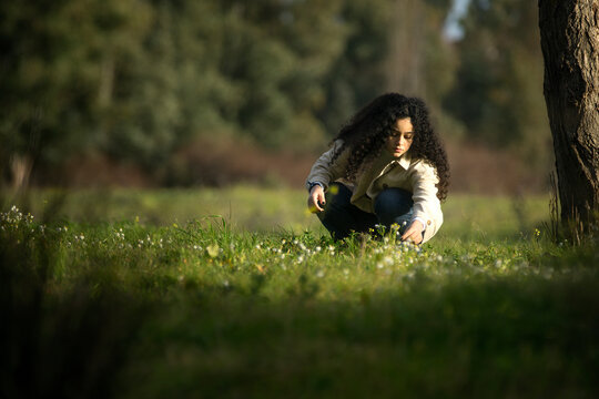Mujer adolescente de pelo largo, moreno y rizoso recogiendo flores silvestres en el campo al atardecer.