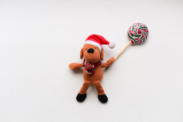 The small toy dog with Santa hat holding two candies. High quality photo
