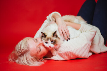 Young woman hugs a ragdoll cat on a red background. Love to the animals.