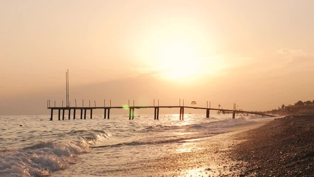 Sea waves, sand beach and pier at golden sunset. Summer vacation in Turkey