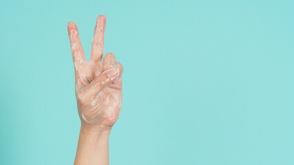 Hand with foam soap bubble is doing Victory or Peace hand Sign on green orTiffany Blue background.