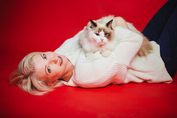 Young woman hugs a ragdoll cat on a red background. Love to the animals.