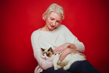 Young woman hugs a ragdoll cat on a red background. Love to the animals.