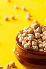 Uncooked chickpea beans on ceramic bowl on yellow background. This legume high in vegetal protein and perfect for vegetarian diet.