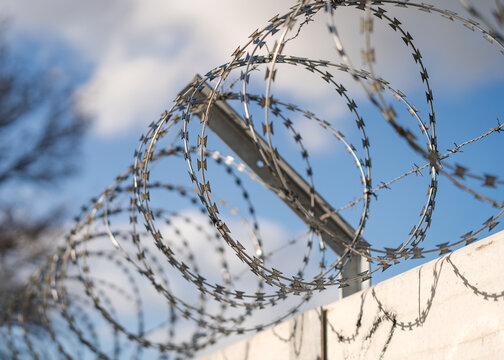 Close up sharp pointed razor wire barb fence coiled on top of prison wall keeping secure prisoners in and criminals out of boarder perimeter
