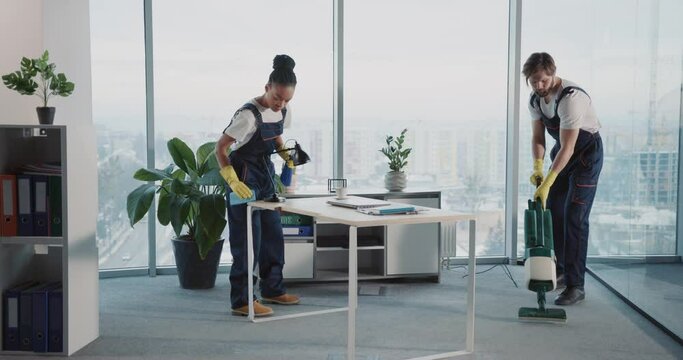 Janitor team of multi-ethnic people cleaning corporate office company room. Young caucasian manin uniform using vacuum cleaner.