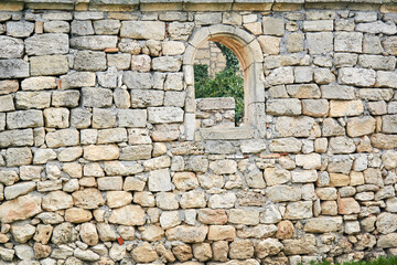 Fototapeta na wymiar stone wall of an ancient building with a semicircular window, beyond which other ruins are visible