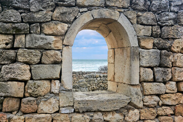 Fototapeta na wymiar window opening in the ruins of an antique wall, behind which you can see the sea