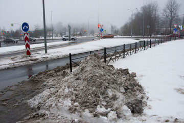 A pile of dirty snow, removed from the highway, lies next to the road. Environmental pollution