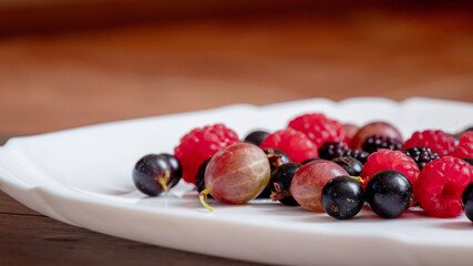 Assorted berries of raspberries, gooseberries, currants on a white plate