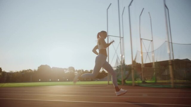Beautiful Female Athlete in Light Blue Sports Top and Leggings Running Extremely Fast in an Outdoors Stadium