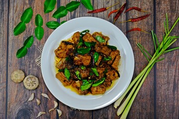 Stir fired pork rips with chilli, lemongrass and kaffir lime leaves surrounded by key ingredients on wooden table. Authentic Thai food.