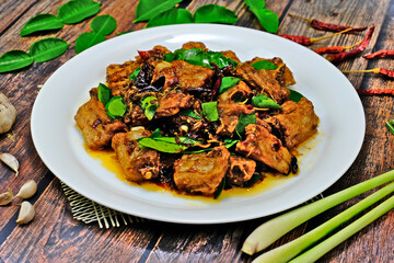 Stir fired pork rips with chilli, lemongrass and kaffir lime leaves surrounded by key ingredients on wooden table. Authentic Thai food.