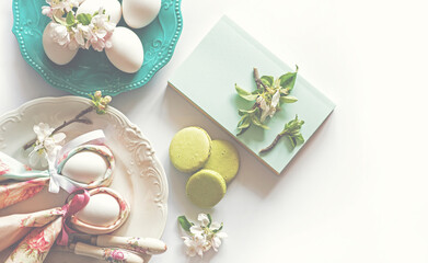 Easter background with easter eggs cute bunny, book, macaroons and spring flowers. Spring still life scene. Vintage pastel styled photo. Festive decoration. Happy Easter! Copy space for you text.