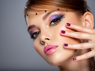 Fototapeta premium Portrait of a beautiful woman with bright makeup. Closeup female face with purple eye make-up. Pretty, sexy girl with violet nails near face. Stylish fashion model with a short slick hair
