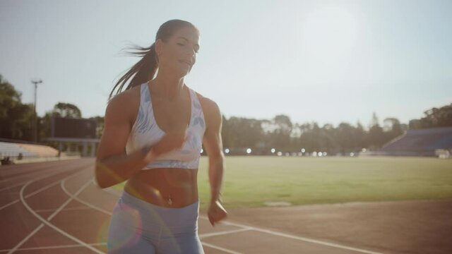 Beautiful Athlete in Light Blue Sports Top Running in an Outdoors Stadium. She is Sprinting on a Warm Summer Afternoon. Finess Woman Doing Her Jogging Training. Slow Motion Portrait Footage.