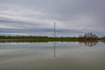 High voltage power line and tower reflecting in a deep water channel 