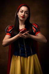 A girl in a princess costume holds a red apple. A brunette. Fairy tale. Red lipstick.