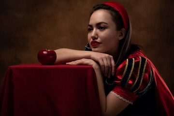 A girl in a princess costume with a red apple. A brunette. Fairy tale. Red lipstick.