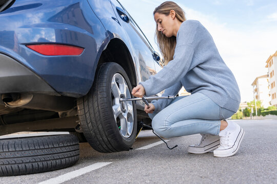 Young beautiful female using force trying to unscrew the wheel bolts nuts with the car jacked up changing wheel..Replacement winter summer season tires ,repairing and maintenance concept lifestyle