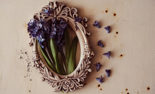 Easter background with Oval ornate vintage frame on rustic background and spring flowers on rustic wooden background. Small flowers fly away from a large cluster of hyacinths.