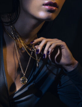 Advertising shooting of jewelry. A young beautiful girl holds in the hand gold chains around her neck. Close-up of the hands and lips.