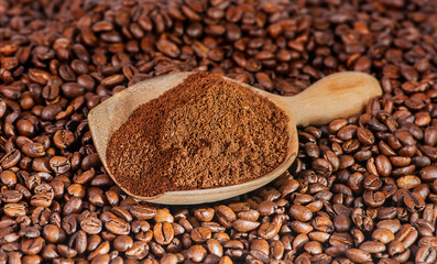 Ground coffee in a wooden spoon on coffee beans.