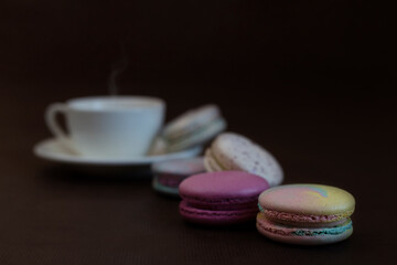 Obraz na płótnie Canvas Small cakes macaroons with almonds and meringues of different colors lie near a cup with hot coffee on a brown background