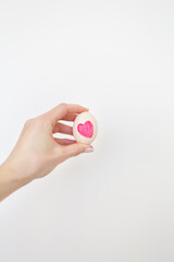 A girl holding an Easter egg with a pink heart painted with watercolors in her hands, isolated on a white background.