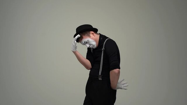 Portrait of cheerful thoughtful male mime ponders scratching head, touching hand to chin, looking at camera. Talented actor wearing hat and gloves showing pantomime on white isolated background.