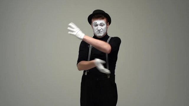 Portrait of offended unhappy male mime folding hands on chest and looking disgruntled at camera. Talented actor wearing hat and gloves showing pantomime on white isolated background.