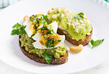 Vegetarian breakfast. Sandwich with avocado puree, boiled eggs and sandwich cream cheese, kiwi, nuts.  Healthy breakfast or lunch.