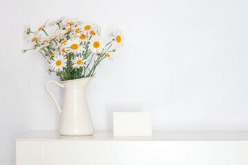 a bouquet of wild flowers in a white vase on the table, retro style, chamomile in a white interior, background for mom's day, free space