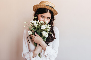 Trendy asian girl sniffing flowers. Romantic brunette young woman holding bouquet of white eustomas.