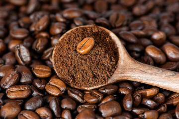 Ground coffee in a wooden spoon on coffee beans.