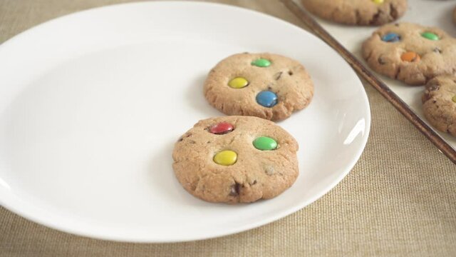 Cookies with colorful M&Ms candies are placed on a white empty plate
