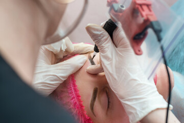 Beautician makes permanent make up correction of the shape of the eyebrows to a young beautiful...