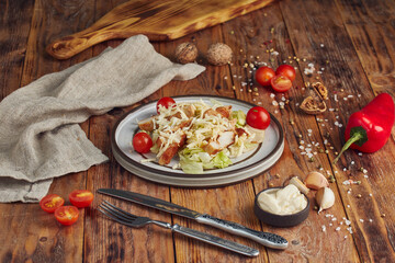 Caesar salad with chicken in a white plate on a wooden background