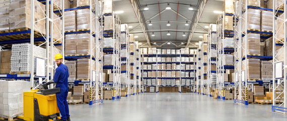 Huge distribution warehouse with high shelves and forklift with young driver.
