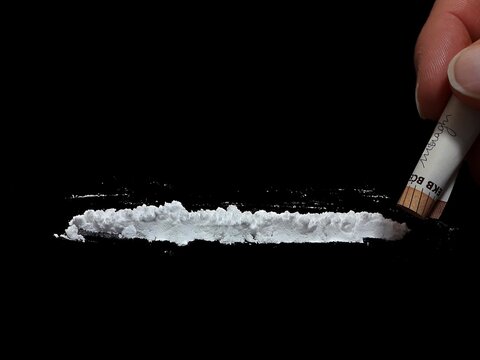 Man use 50 euro banknote to snorting cocaine drug powder lines on black table